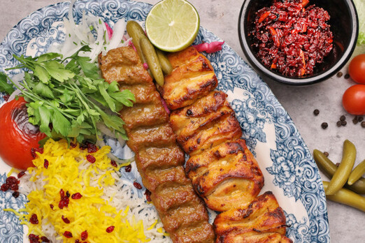 Kebab Koobideh und Joje Kebab bei Imbiss SADAT in Graz – frisch gegrillte Fleischspieße und Hühnerkebab mit Basmatireis, Kräutern, gegrillter Tomate und traditionellen Beilagen auf einem orientalischen Teller.