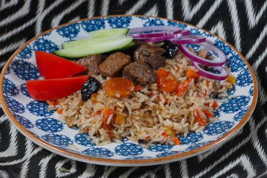 Qabuli Polo bei Imbiss SADAT in Graz – traditionelles afghanisches Reisgericht mit Basmatireis, Karotten, Rosinen und zartem Fleisch, serviert auf einem orientalischen Teller mit frischem Gemüse.